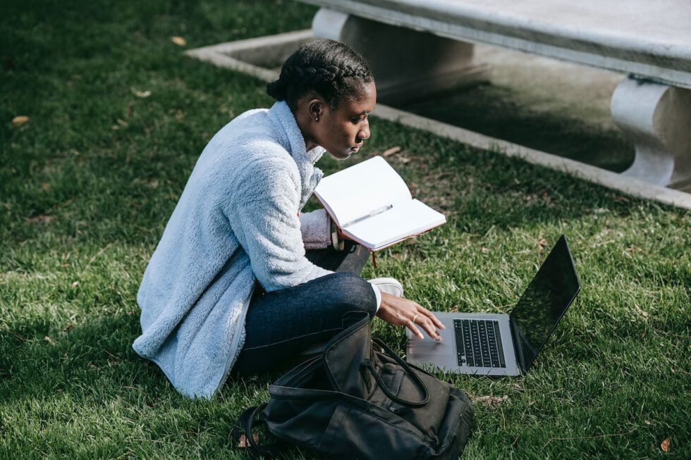 black female student using computer in grass