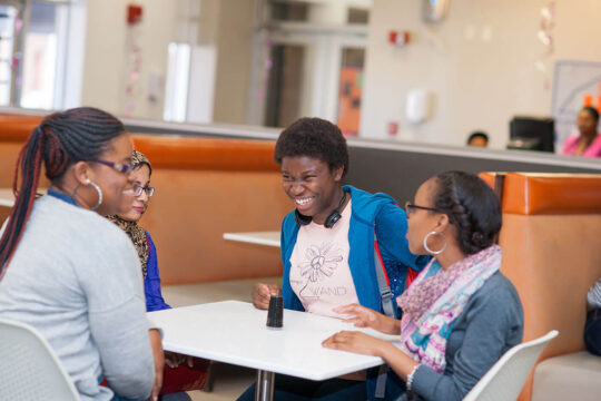 four students in dining area smiling with books